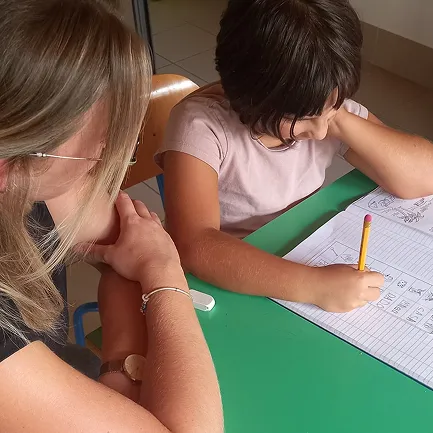 Un'educatrice del doposcuola che osserva e supporta una ragazza mentre fa i compiti.