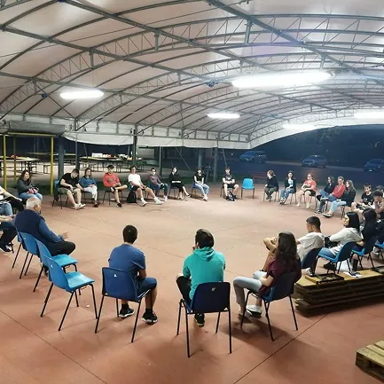 Un gruppo di giovani a sentire Don Daniele Fort mentre stanno seduti in cerchio sotto una tenda nel centro pastorale GP2 di Porcia.